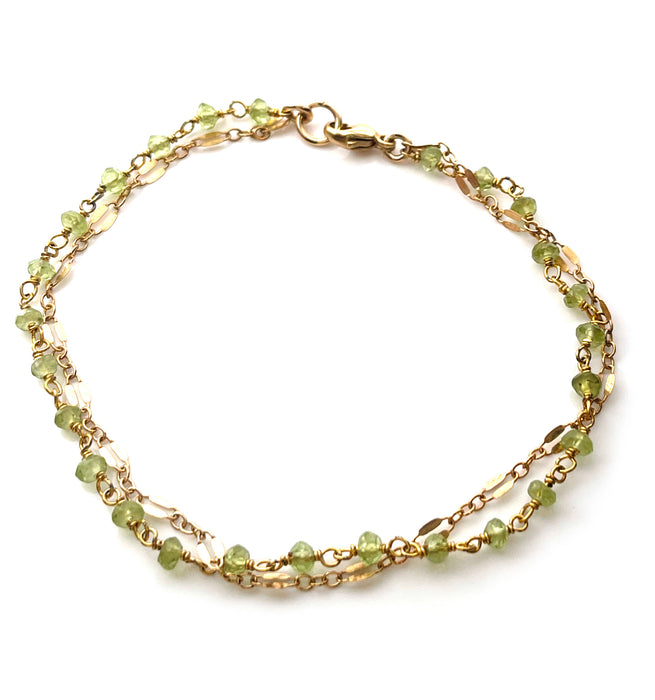 a close up view of a handmade peridot and 14k gold chain bracelet on a solid white background
