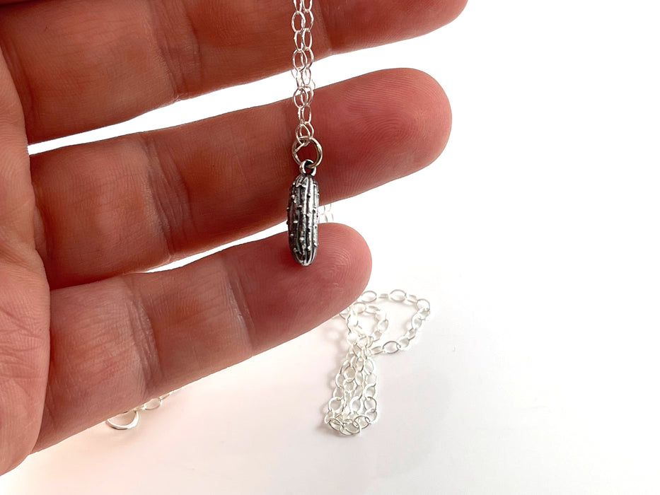 sterling silver pickle charm necklace being held in a hand to demonstrate size