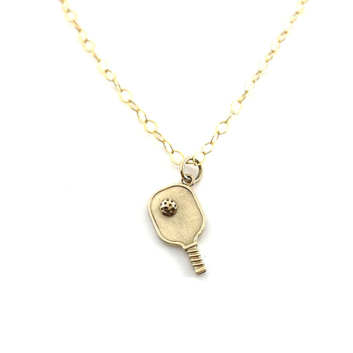 a close up view of a gold pickleball paddle charm on a delicate gold chain