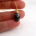 Gold necklace with a black faceted pendant held between fingers on a white background