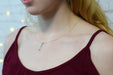 a silver rainbow vertical bar pendant on a silver chain hanging just below the collar bones of a model with red hair in a burgundy tank top