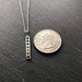 a close up of a rainbow chakra pendant on a silver chain next to a USD quarter to demonstrate size