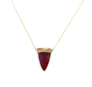 a close up shot of the detailed faceted of a red quartz pendant that is wire wrapped by hand and attached to a gold necklace chain on a solid white background