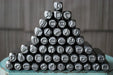 A pyramid arrangement of black metal letterpress printing stamps with various engraved symbols, displayed on a distressed teal wooden surface against a gray wooden background.