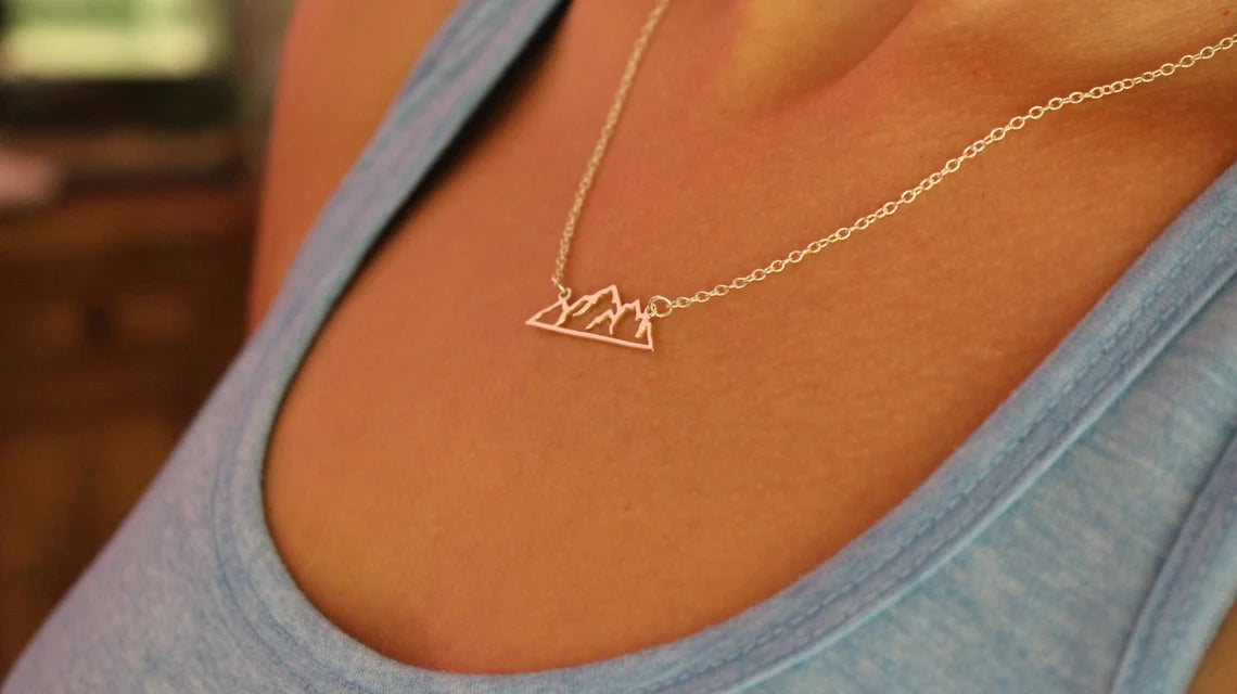 Silver mountain landscape cutout necklace on a lady in blue tank top, very close up view of collar bones