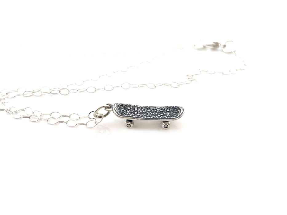 close up view of a sterling silver skateboard charm necklace on a solid white background