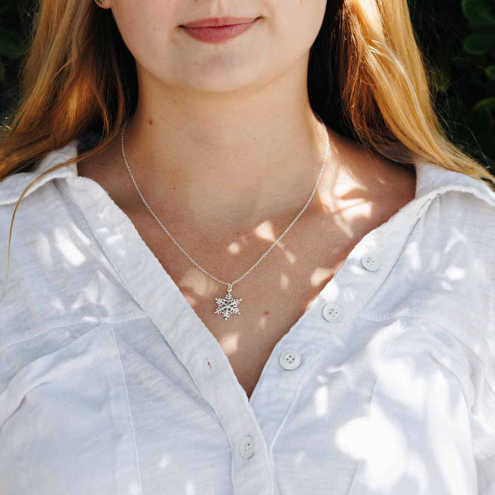 a view of a young lady in a white blouse wearing a sterling silver snowflake charm necklace 