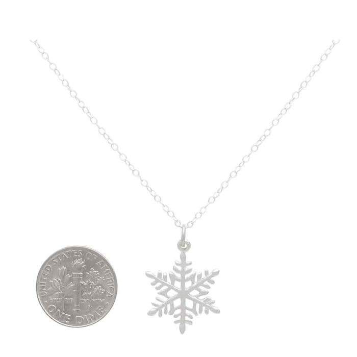 a close up of a sterling silver snowflake charm on a silver chain next to a USD dime to show size. 