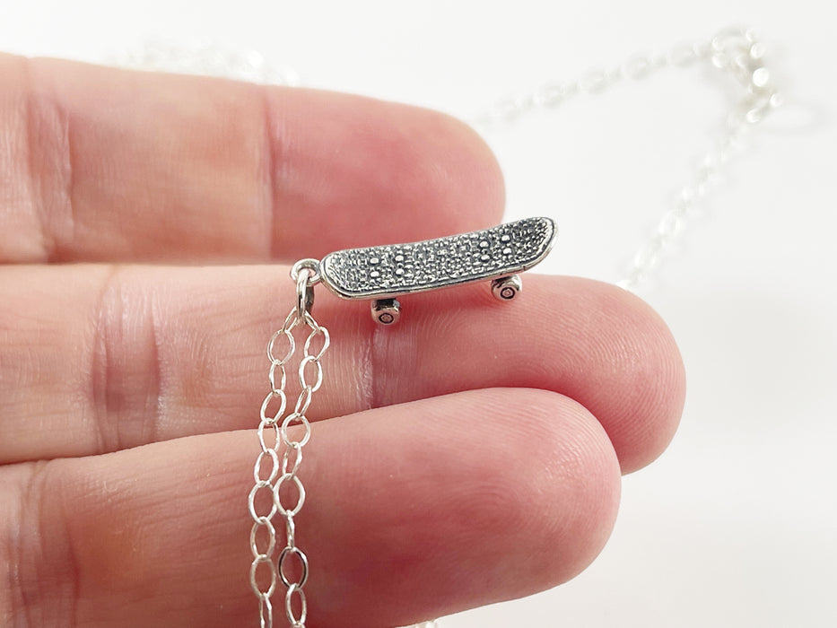 three fingers holding a sterling silver skateboard charm necklace to showcase detail and size