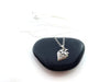 a sterling silver strawberry charm necklace displayed on a small black stone against a white background.