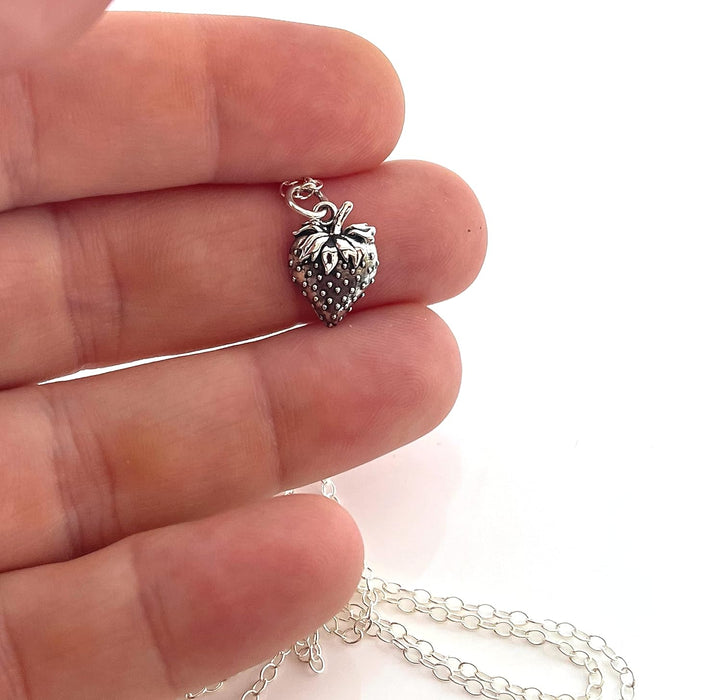 a sterling silver strawberry charm displayed on a few fingers to demonstrate size