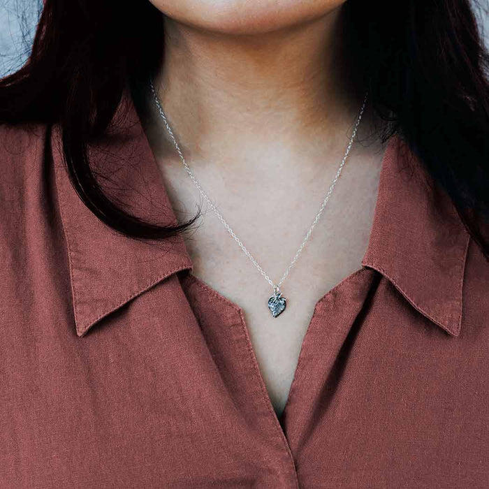 a silver strawberry charm hanging on a silver chain on the neck of a fair-skinned dark hair model.