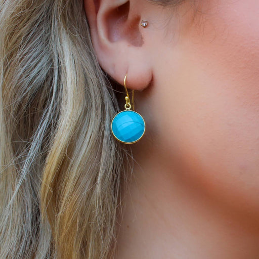 a close up view of a light skinned ladies ear with a circle turquoise gemstone earring in gold vermeil