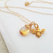 A 14k gold filled necklace with a detailed bee charm and a sparkling citrine briolette pendant, displayed on a white plate.